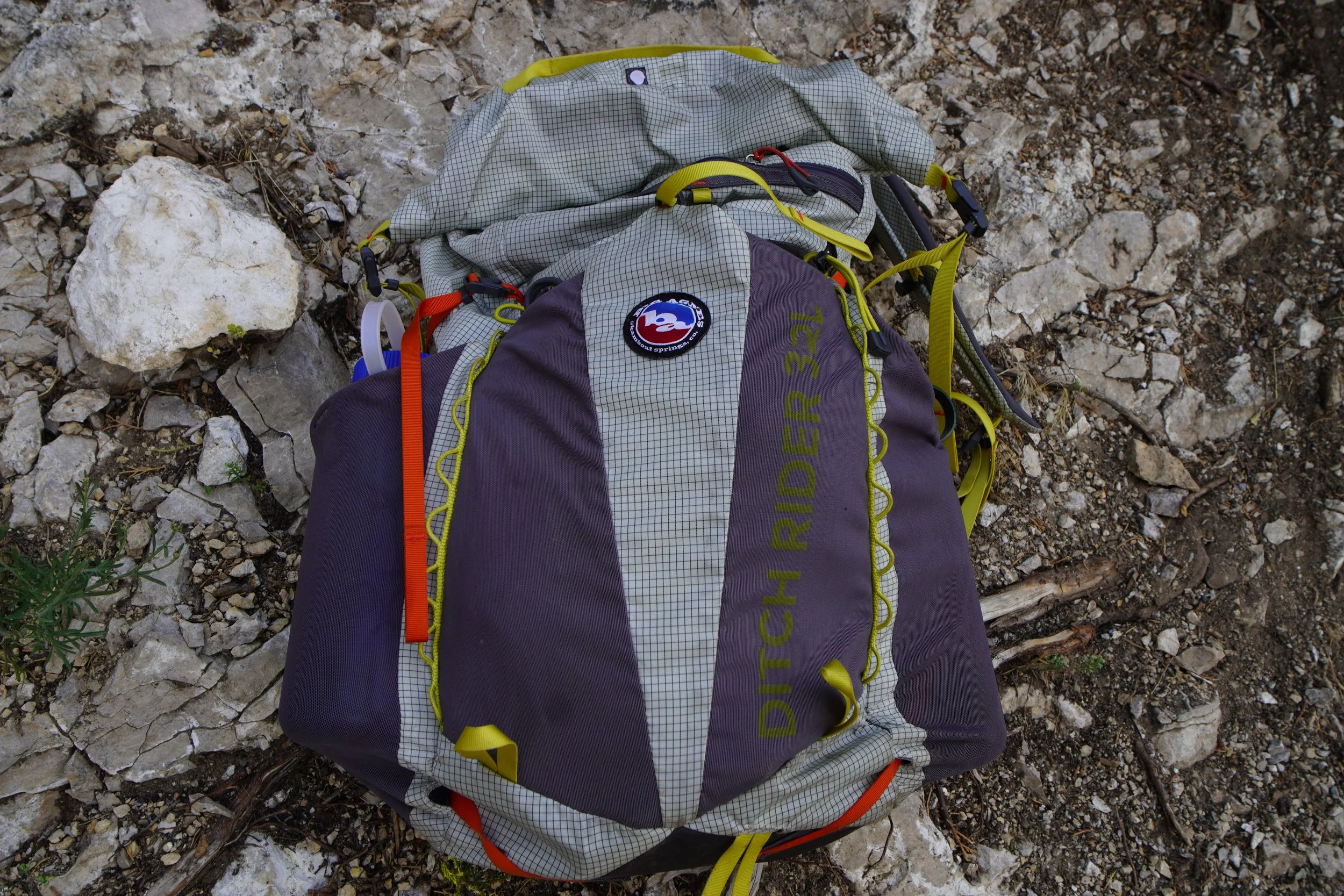 Top view of a gray and yellow hiking backpack labeled "Ditch Rider 32L" placed on rocky ground.
