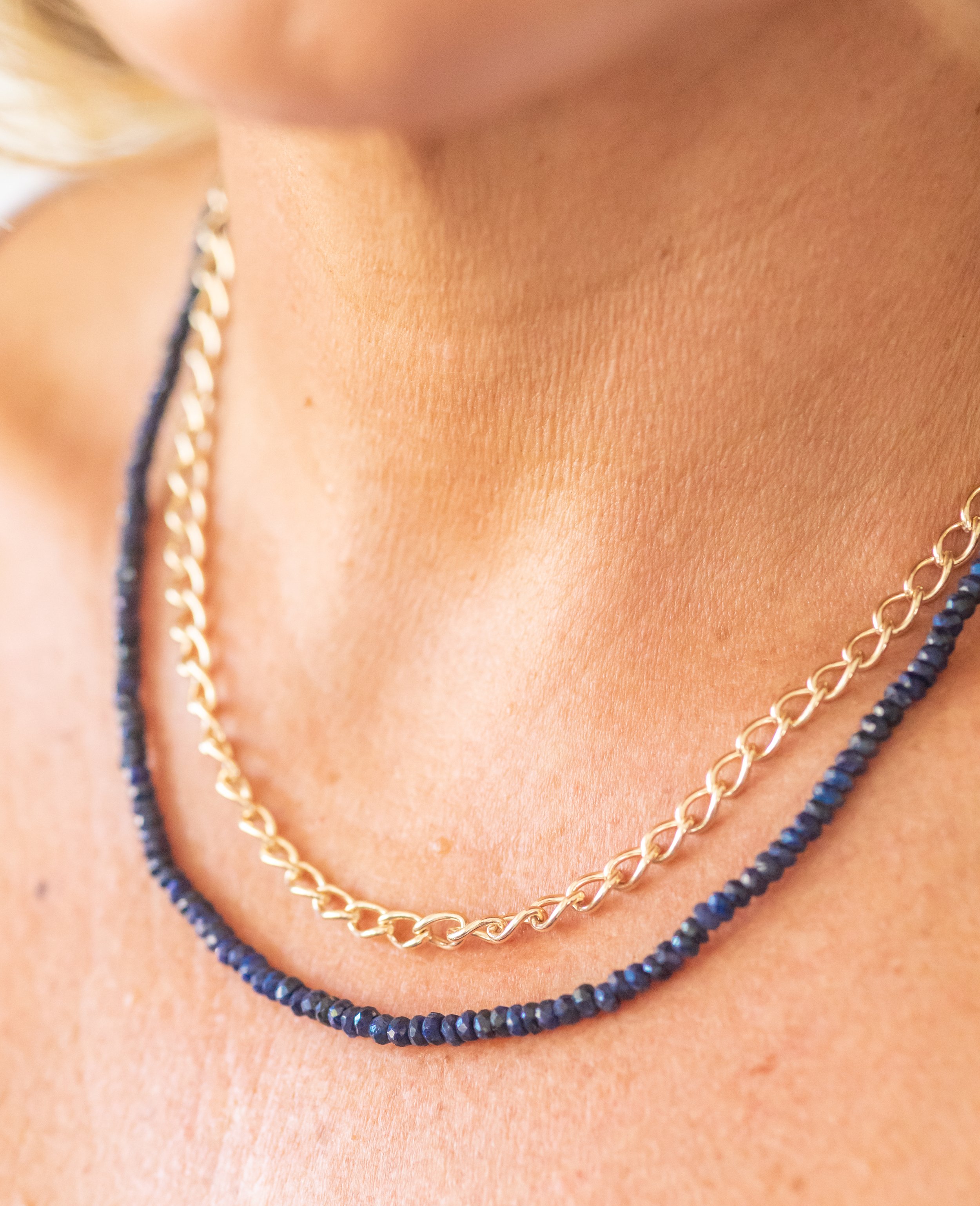 Close-up of a person's neck wearing two necklaces, one gold chain and one dark beaded necklace.