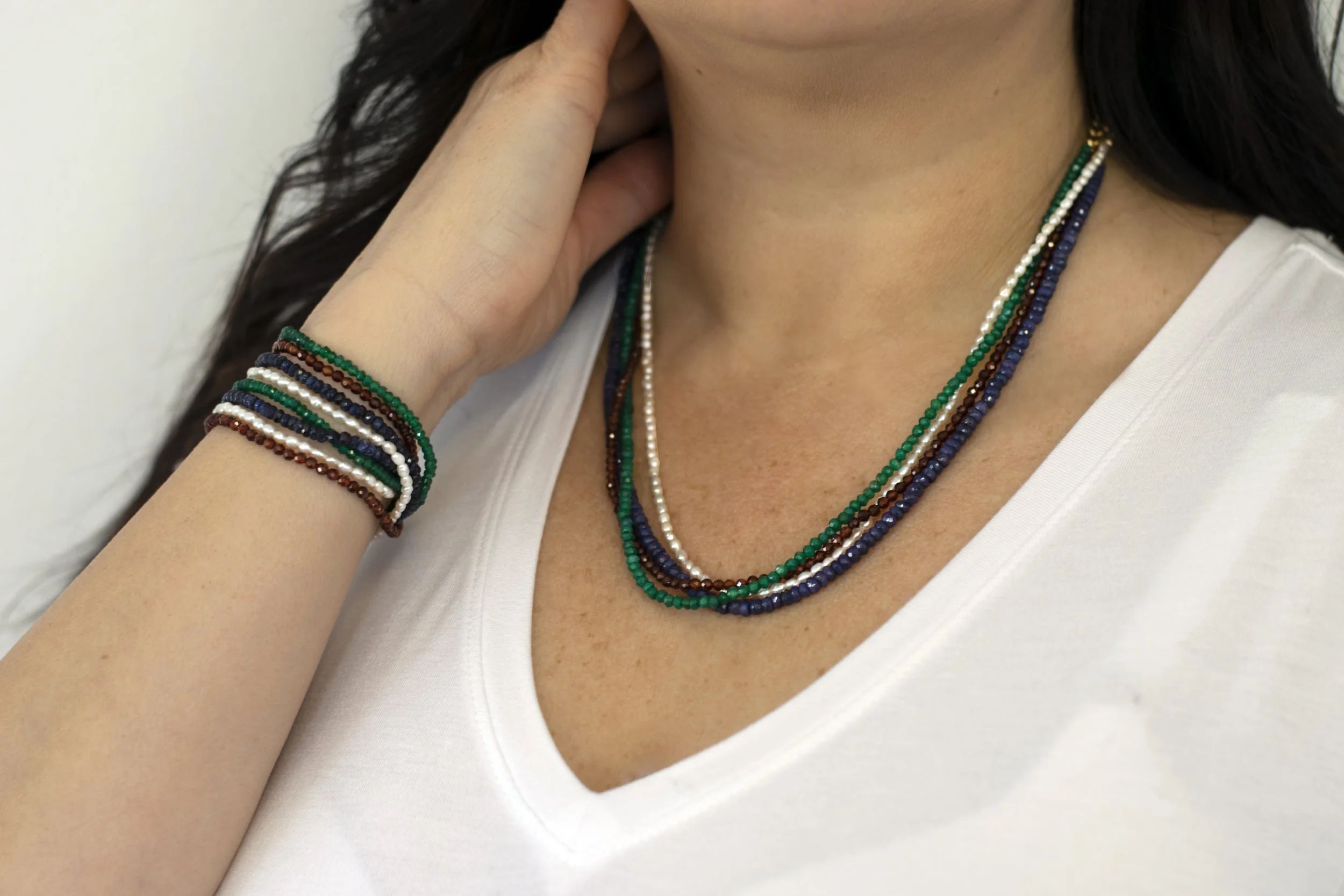 Close-up of a woman wearing multiple layered beaded necklaces and bracelets, dressed in a white top.