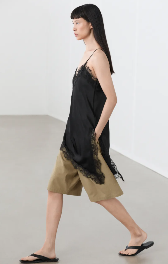 Model wearing Massimo Dutti black asymmetrical lace camisole with beige shorts and black flip flops