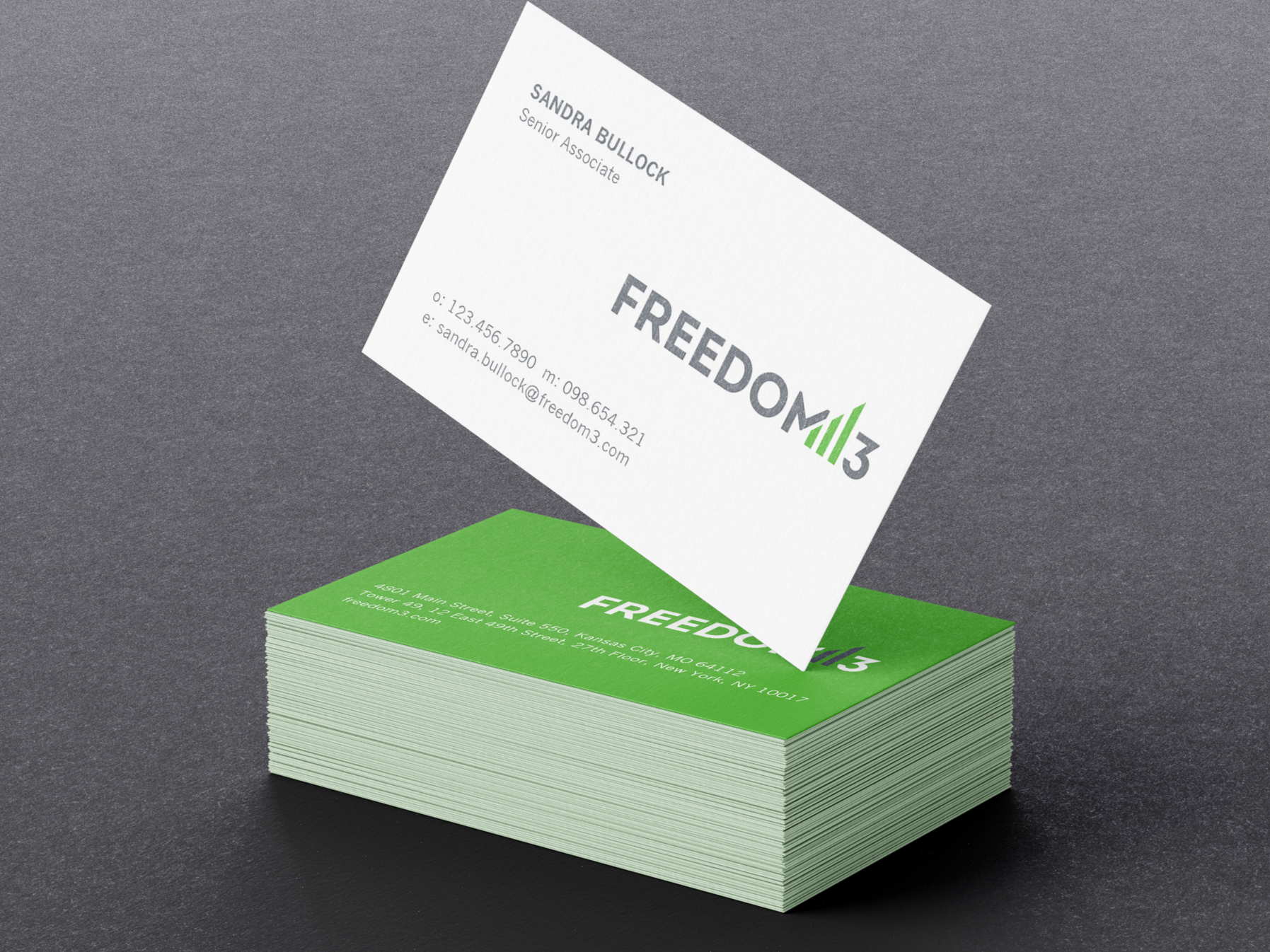 A stack of green business cards with white text and a white business card being lifted off the top of the stack. The cards display contact information and the logo 'FREEDOM13'.