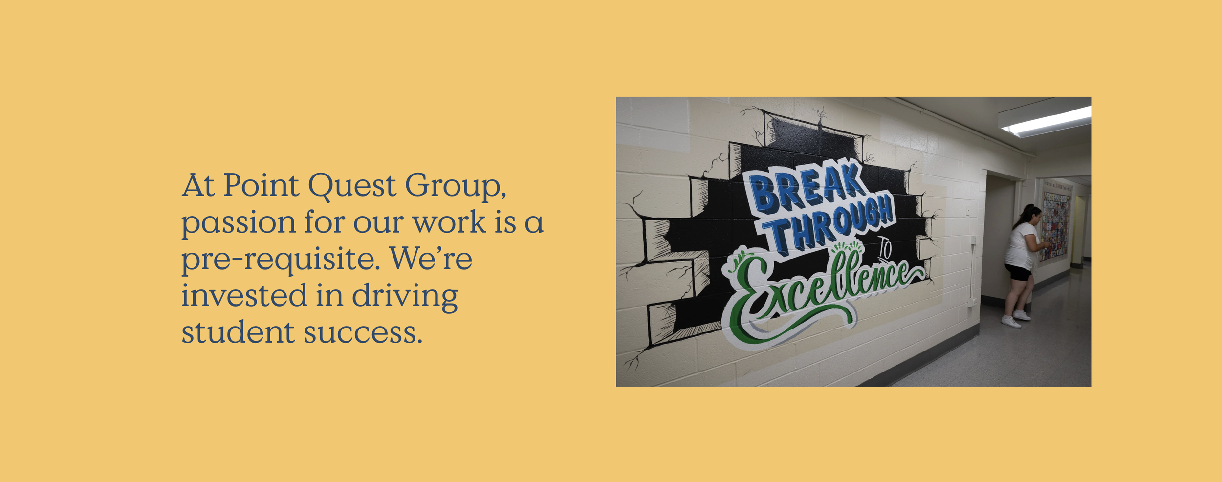 A hallway with a mural on the wall that says 'Break Through to Excellence' in colorful letters. A girl is standing near a bulletin board.