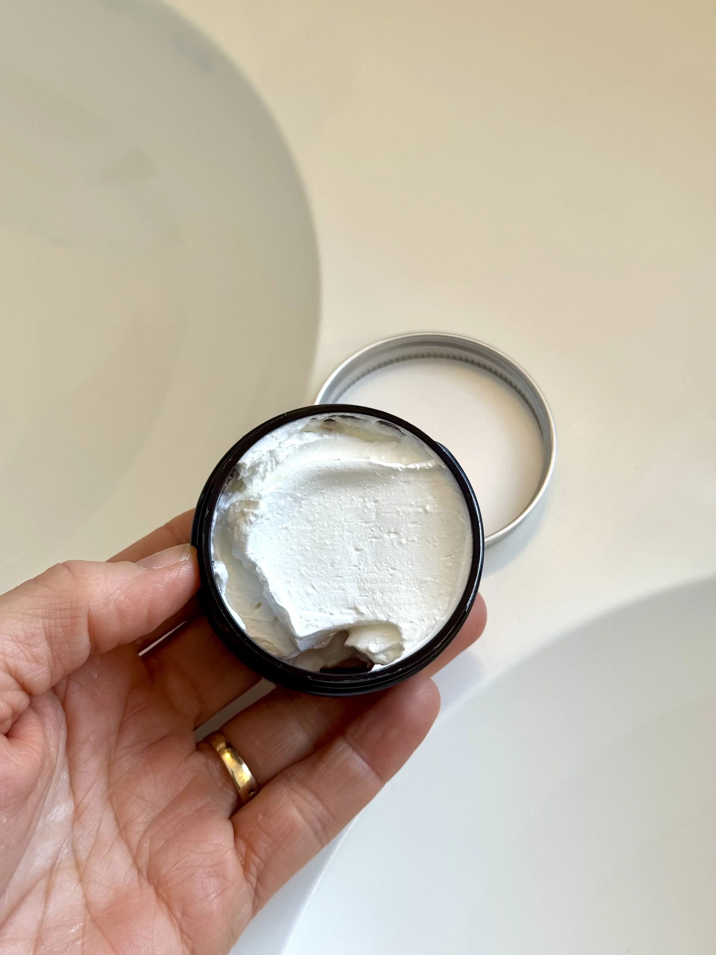 Hand holding a glass jar with a black lid and purple botanical illustration label, in front of a white sink.
