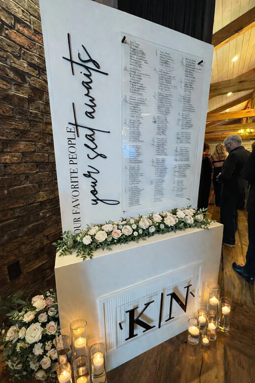 Luxury white and black wedding seating chart setup with a wood box base and inserted wood panel with attached acrylic seating assignment and 3D lettering that says "Our Favorite People Your Seat Awaits"