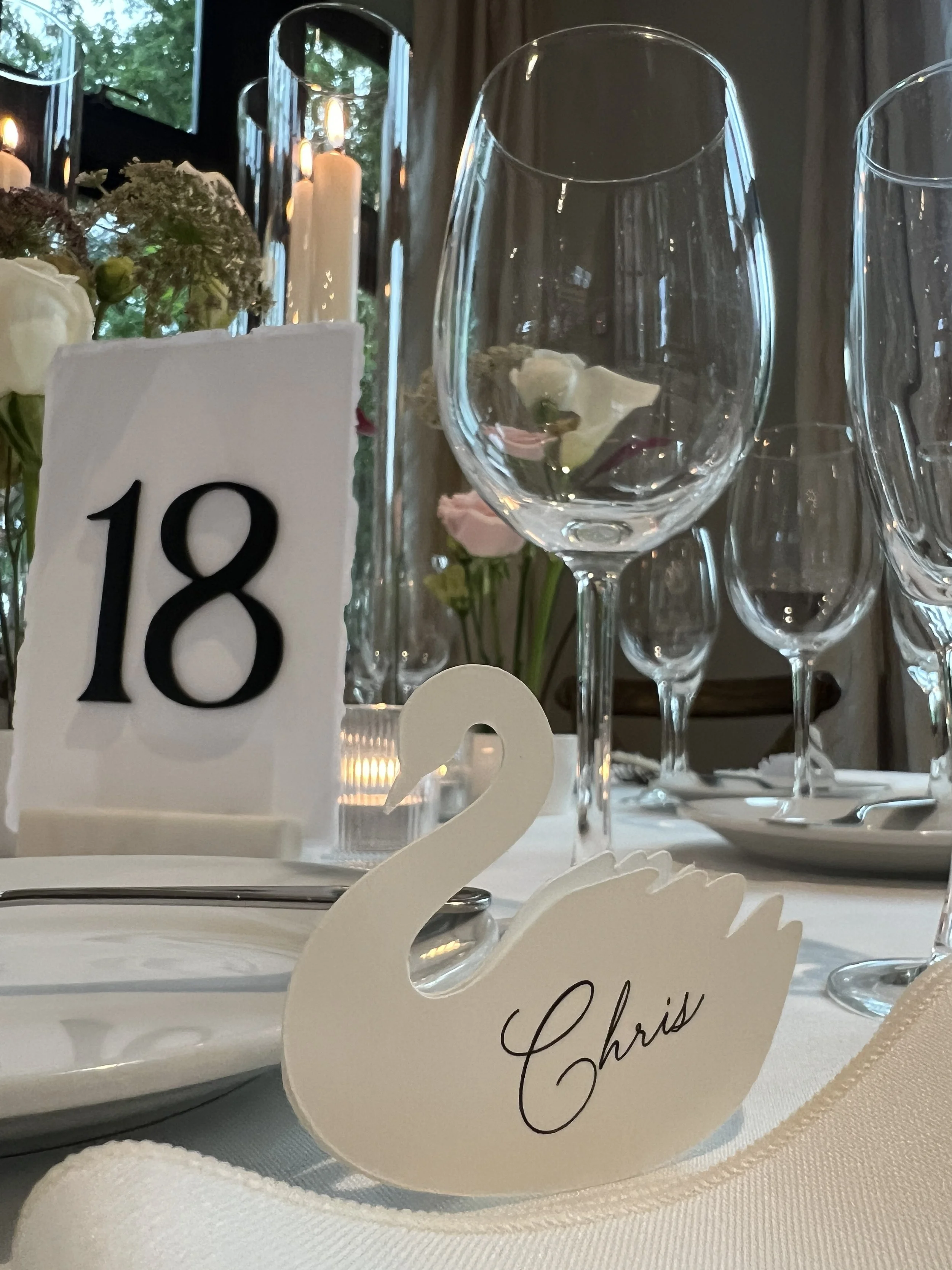Personalized paper swan escort cards in the foreground, with custom raised number table numbers on deckled edge watercolor paper with marble stand