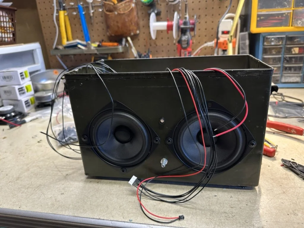 Two speakers with wires on a workbench in a workshop