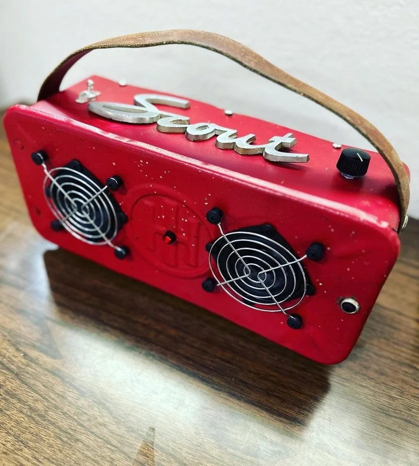 Vintage red radio or speaker box with "Scout" logo, featuring two speaker grills and a leather strap handle on a wooden surface.