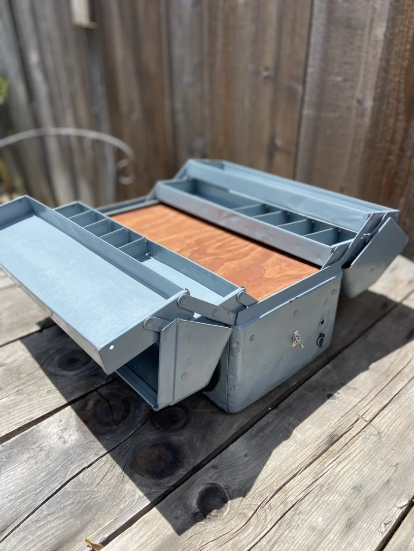 Open metal toolbox with multiple compartments on a wooden surface
