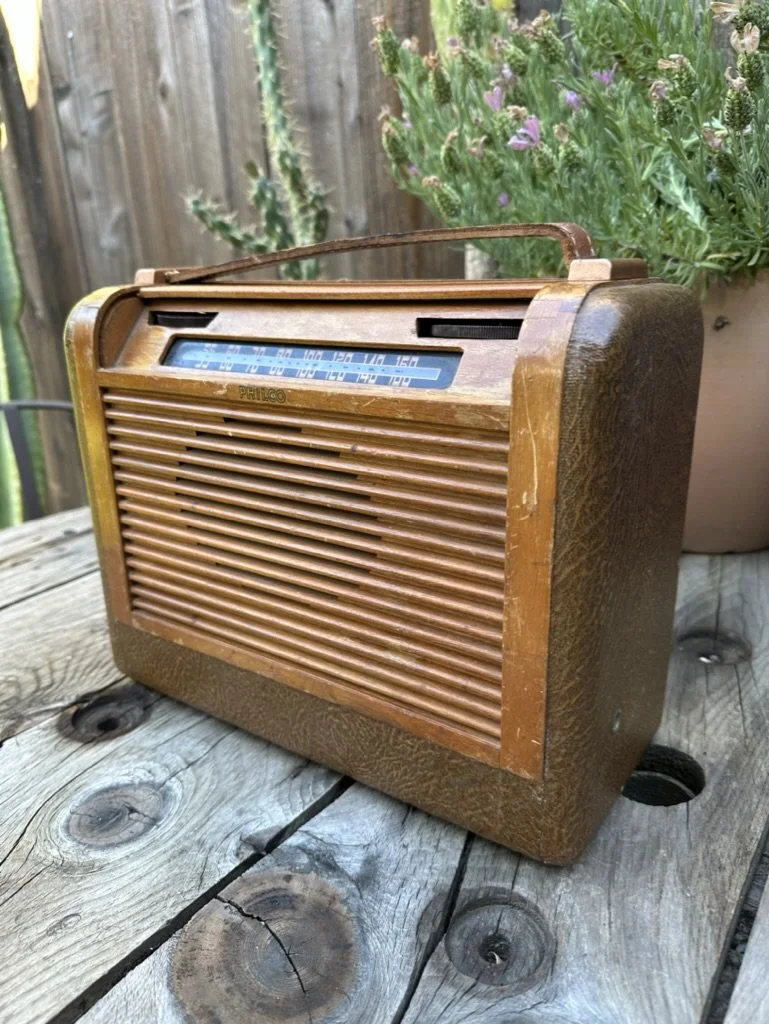Vintage Philco radio on wooden table outdoors with plants in background
