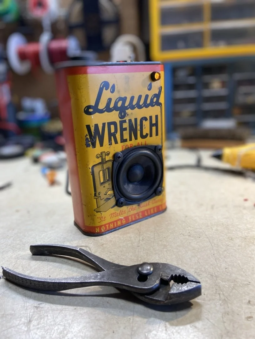 Vintage-style Liquid Wrench can with speaker modification on a workbench, with pliers in the foreground.