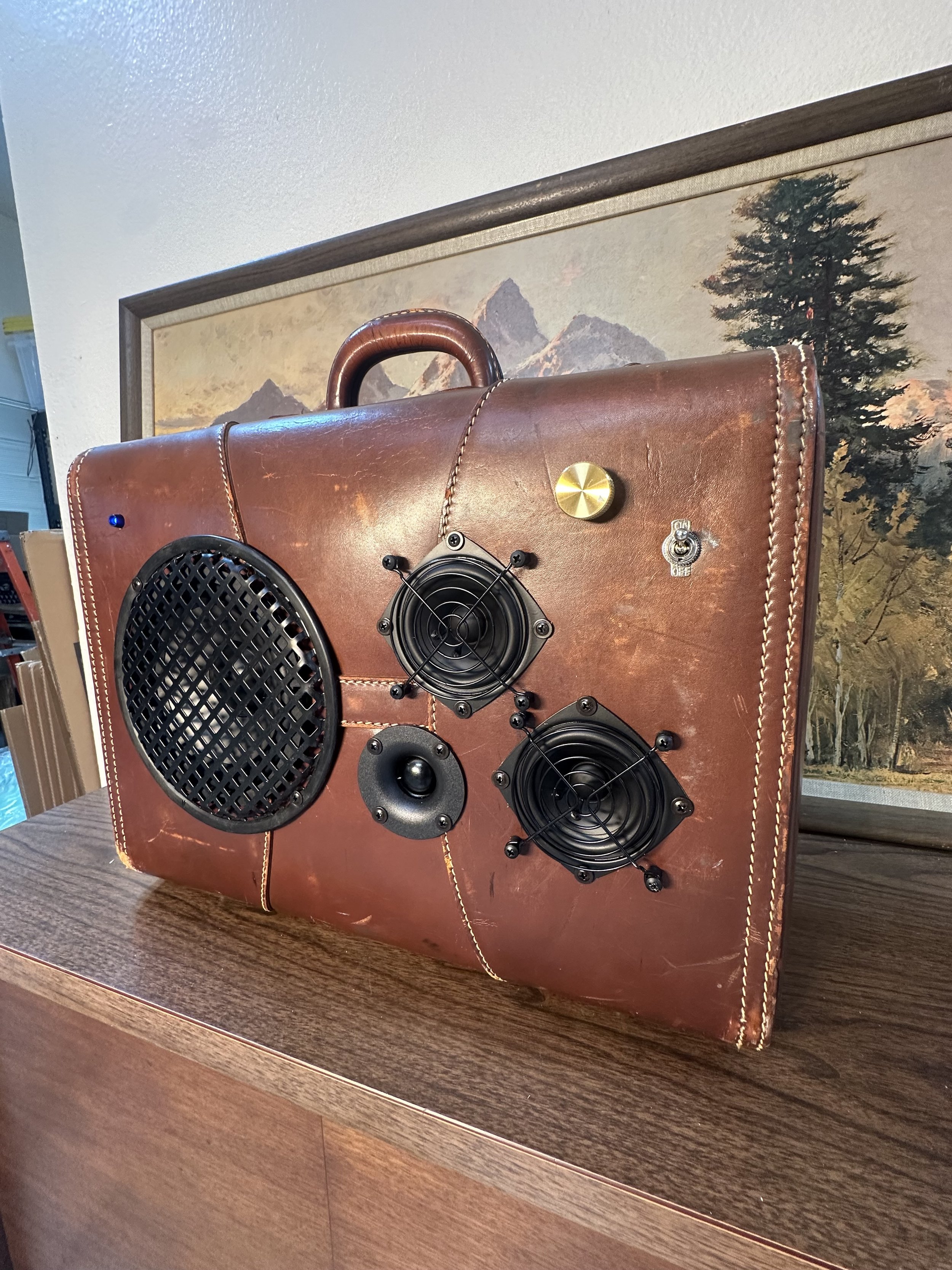 Vintage suitcase converted into a speaker system with multiple speakers and knobs mounted on the front.