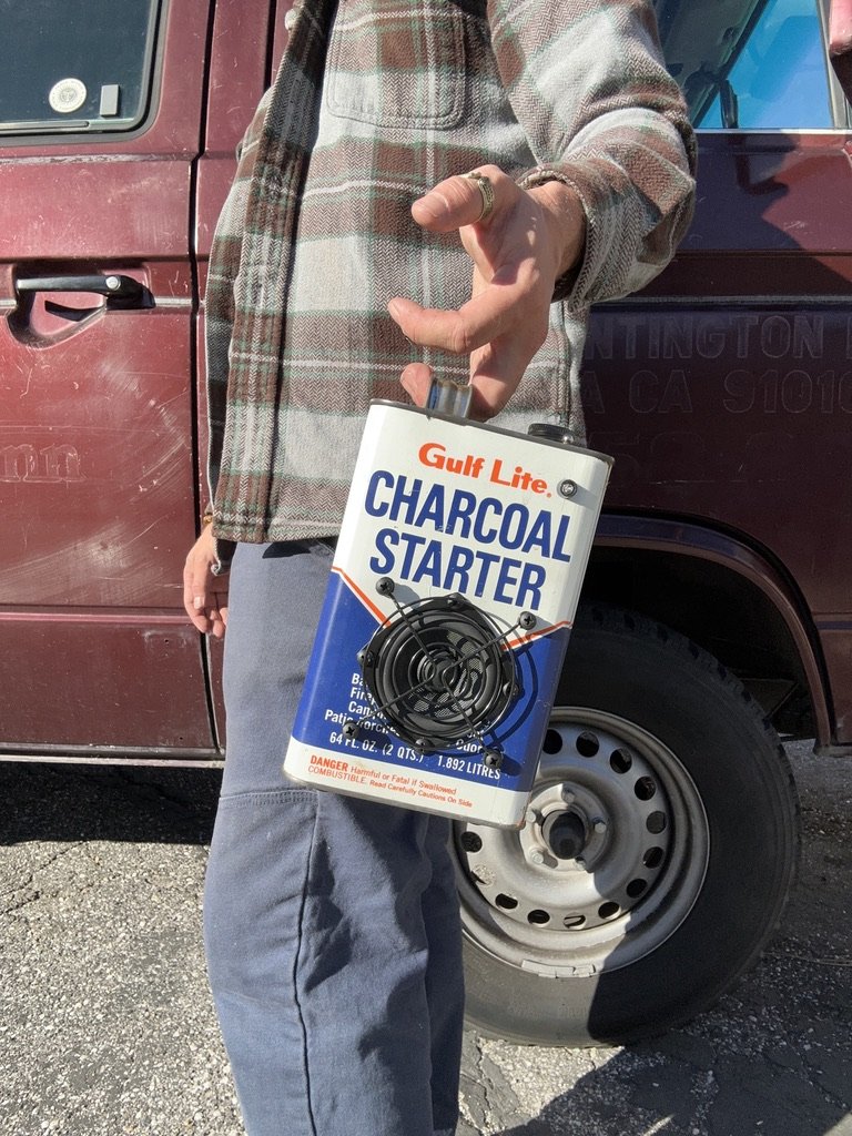 Person holding a can of Gulf Lite Charcoal Starter in front of a maroon van.