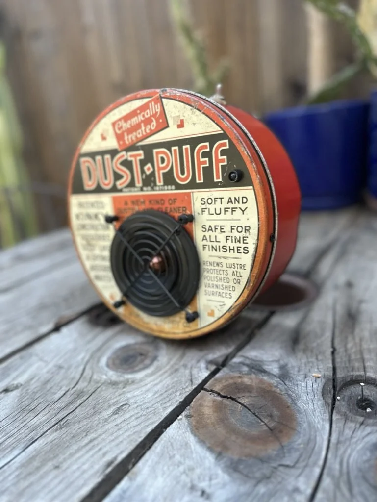 Vintage "Dust Puff" canister on wooden surface, used for dusting and cleaning; labeled as chemically treated and safe for finishes.