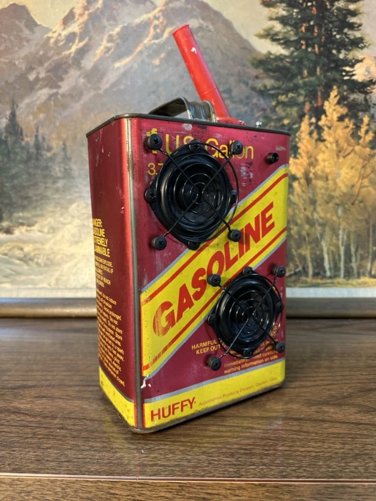 Retro gasoline can with attached speaker elements on display, set against a mountain-themed background.