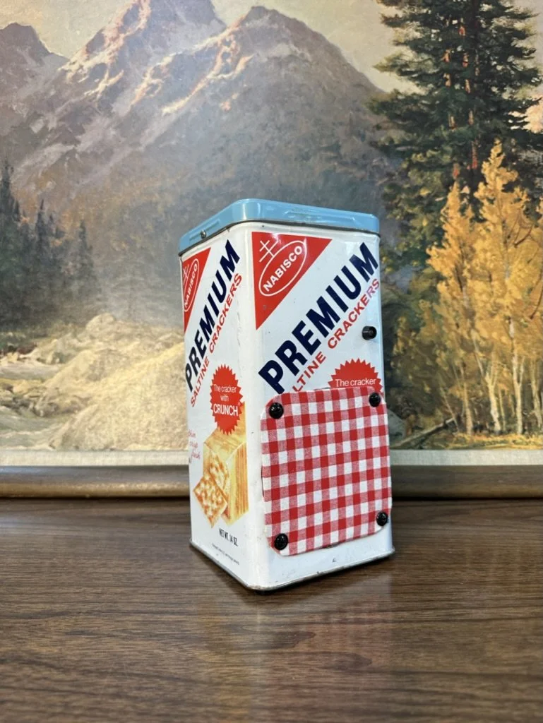 Vintage Nabisco Premium saltine cracker tin with a mountain landscape painting in the background.