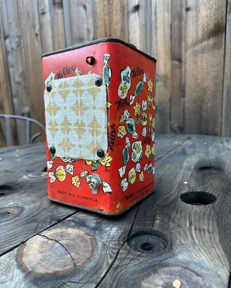 Vintage Heller Candy Company tin with colorful candy illustrations on a wooden table, featuring a fabric-covered speaker-like front.