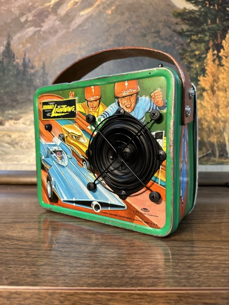 Retro Johnny Lightning lunchbox with a speaker on the front, featuring vibrant vintage car and racer illustrations.