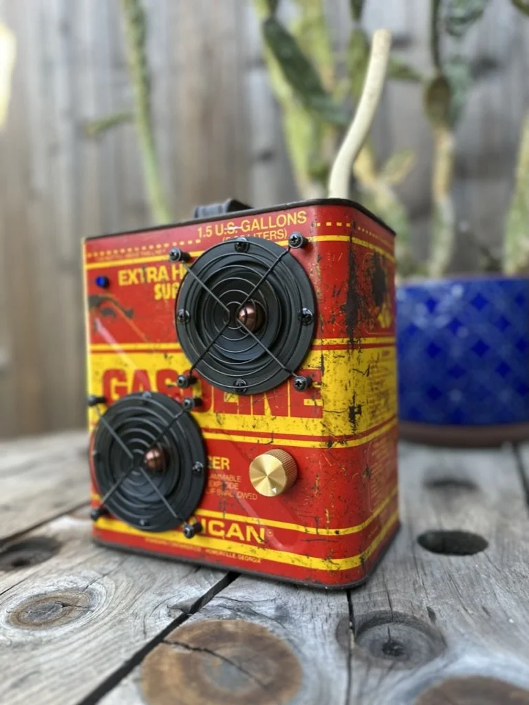 Vintage gasoline can converted into a speaker with two audio components and a control knob, on a wooden surface.