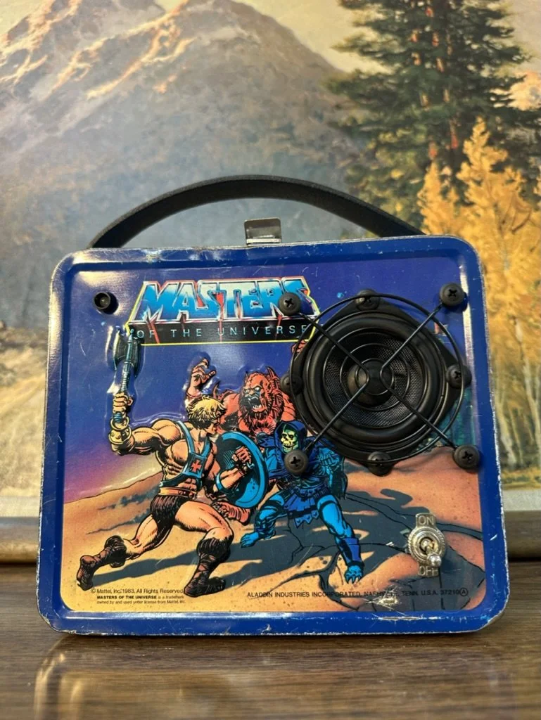 Vintage Masters of the Universe lunchbox featuring He-Man and Skeletor illustration with a speaker, toggle switch, and handle.