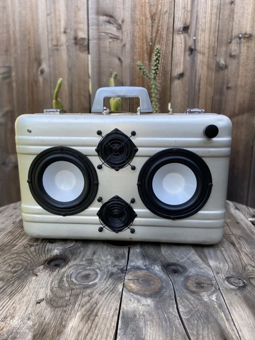 Vintage suitcase converted into a portable speaker system with three speakers mounted on its side.