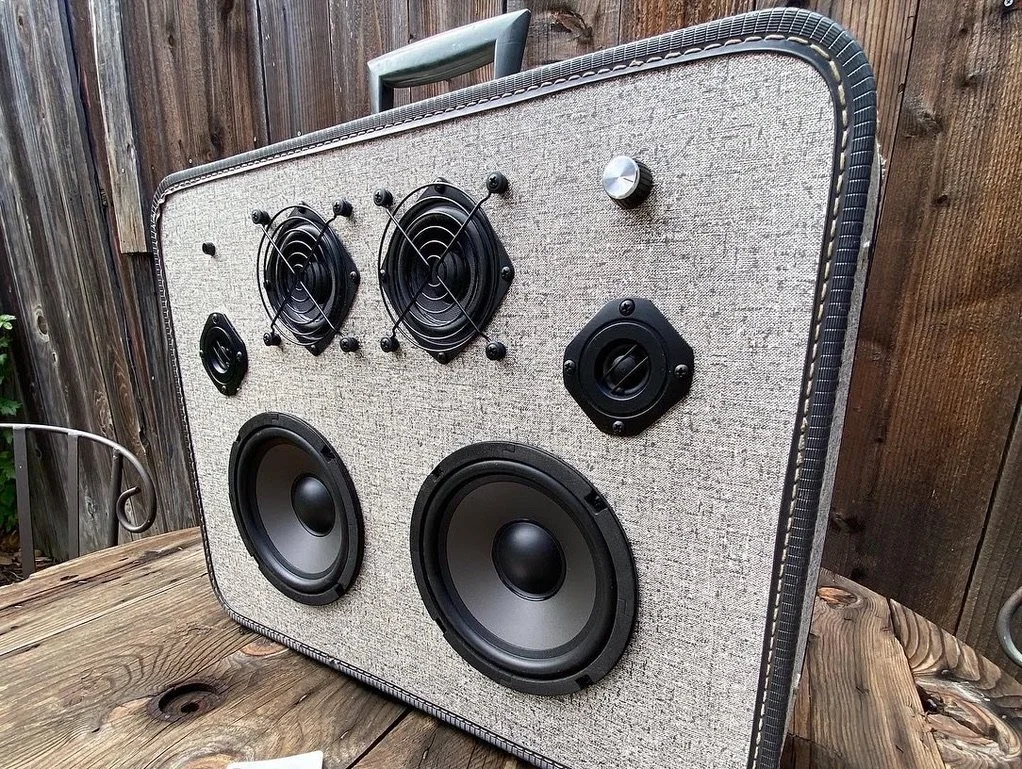 Custom vintage-style portable speaker with multiple drivers on a wooden surface, wooden fence background.