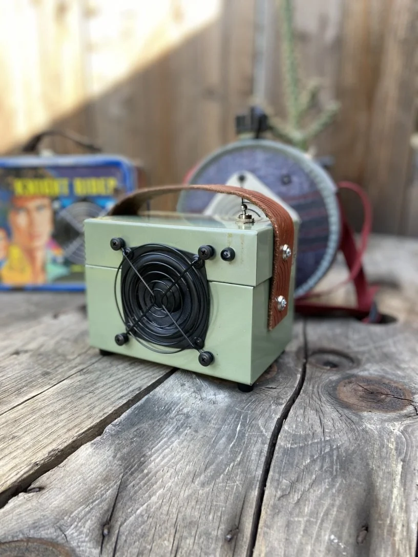 Vintage green and brown speaker on wooden table with retro fan and toy in background.