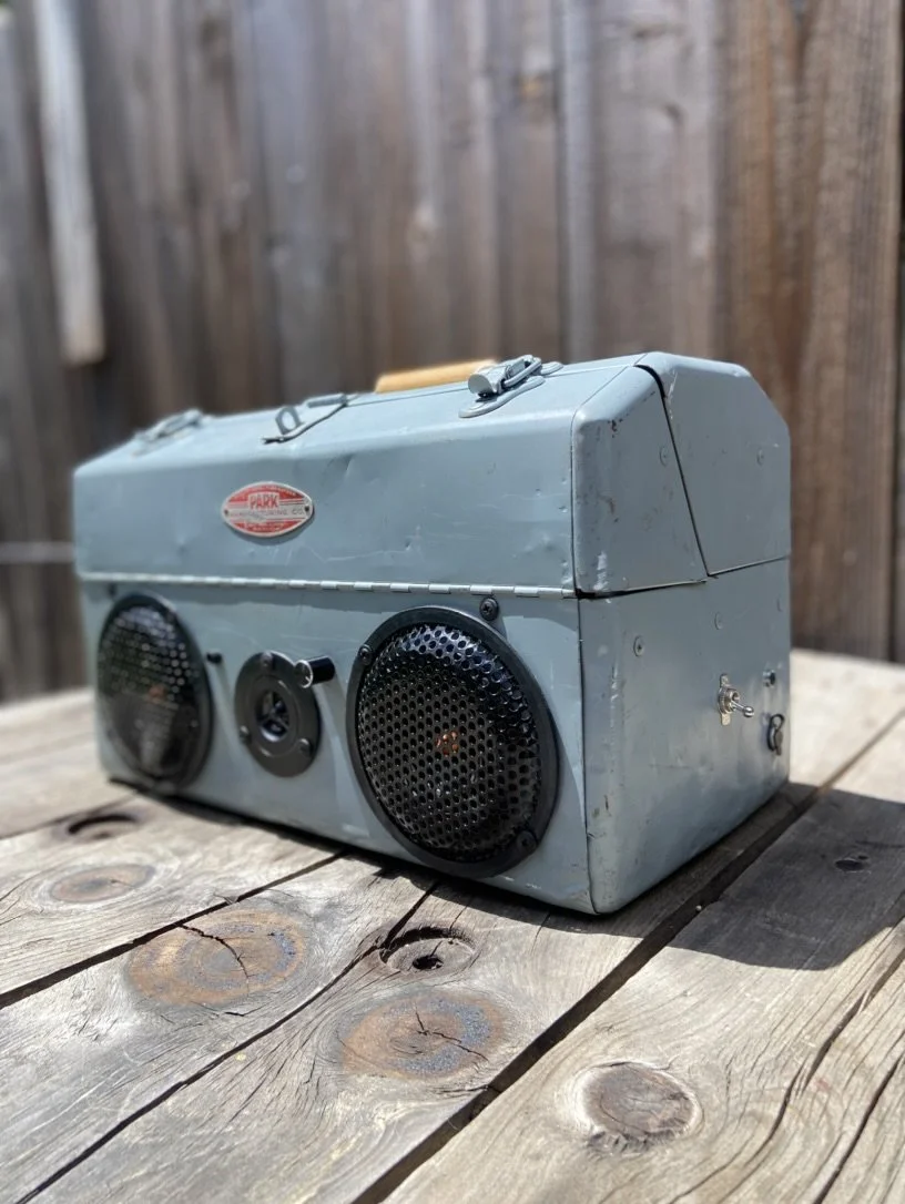 Vintage metal speaker box with round grilles on a wooden surface.