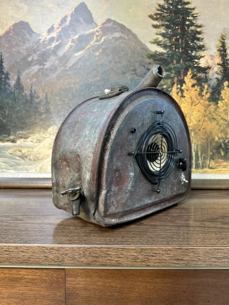 Vintage metal heater with fan on wooden surface, mountain painting backdrop