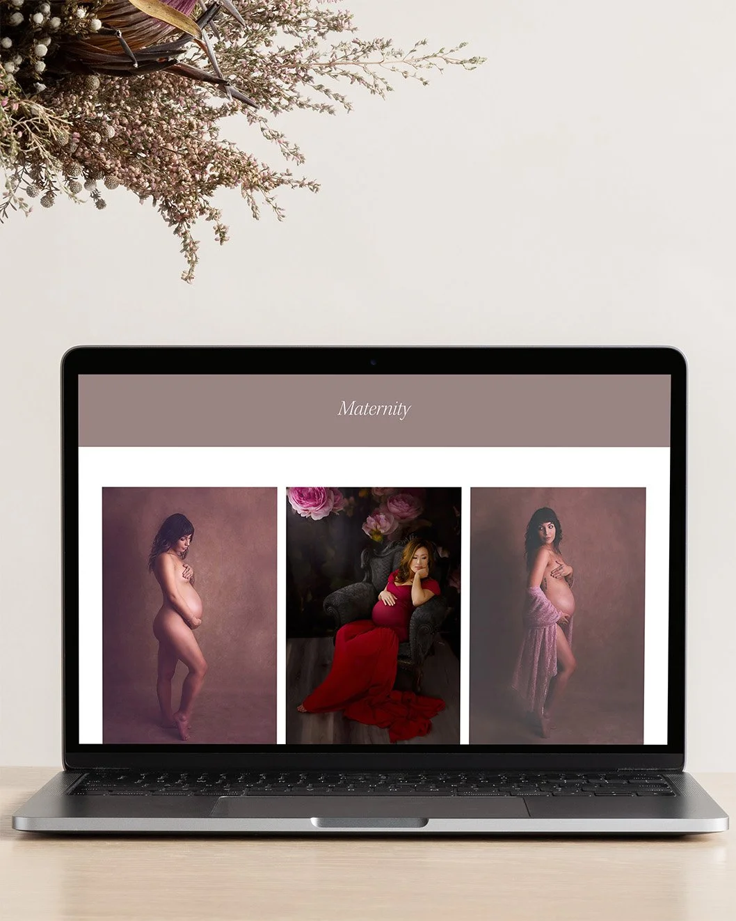 Laptop mockup of maternity photography website on light wood table with flowers in background.