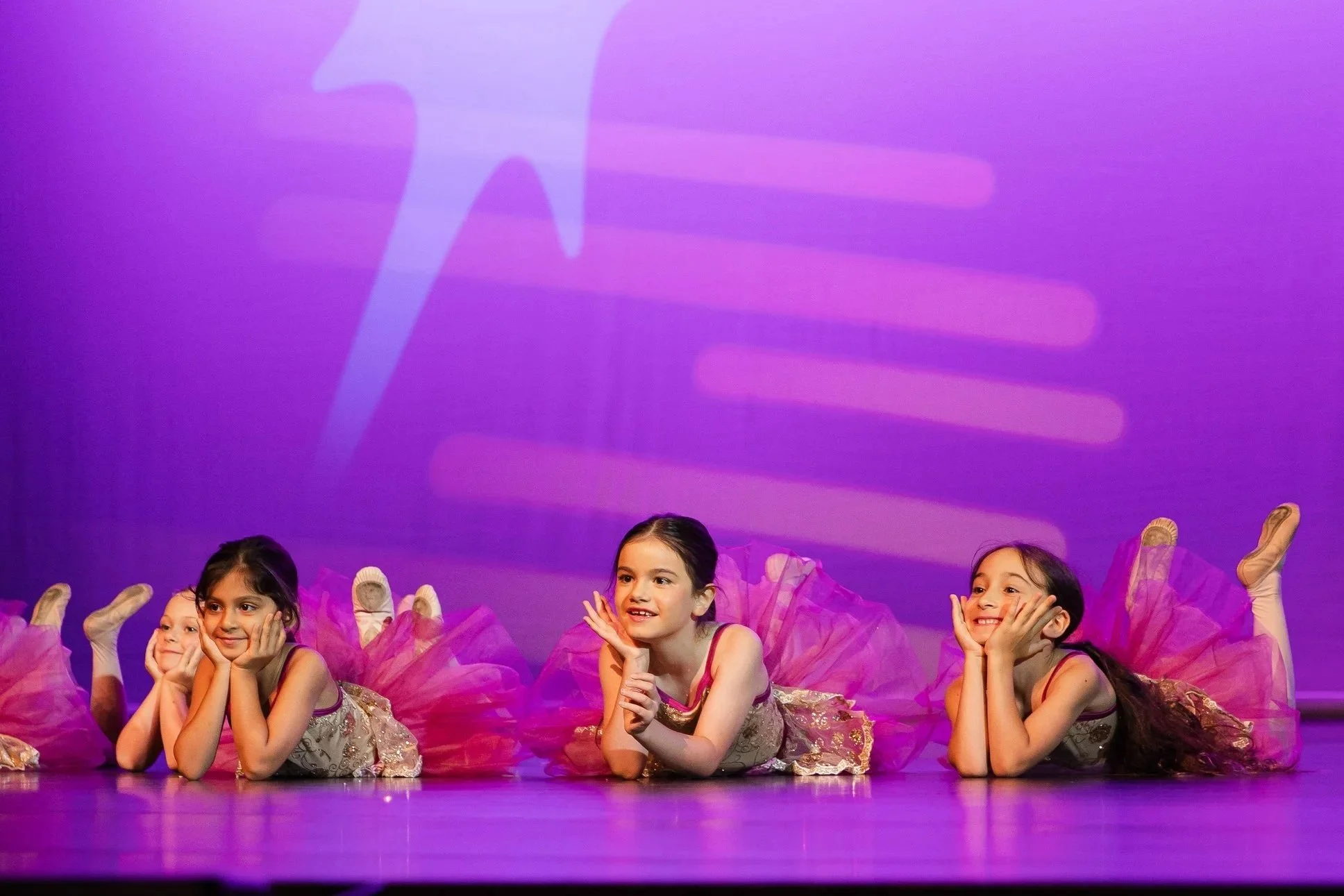 Smiling child in pink dance costume with outstretched arms on stage