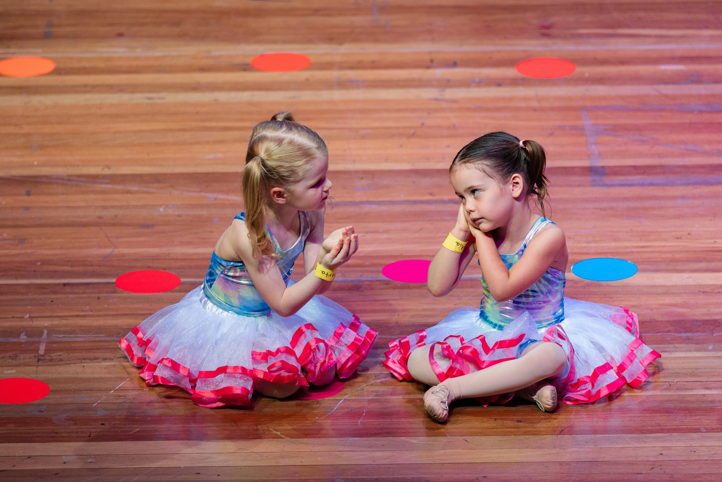 Young girl in colorful dance costume posing on stage with blue curtain background.