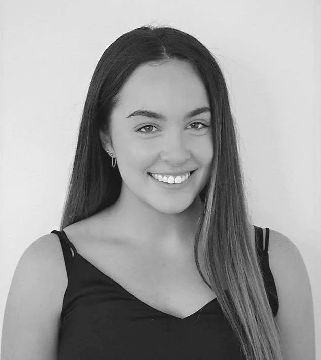 A black and white portrait of a smiling young woman with long hair, wearing a sleeveless top.