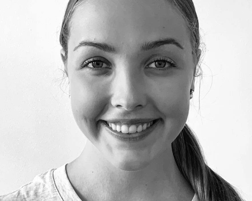 Black and white portrait of a smiling person with long hair tied back.