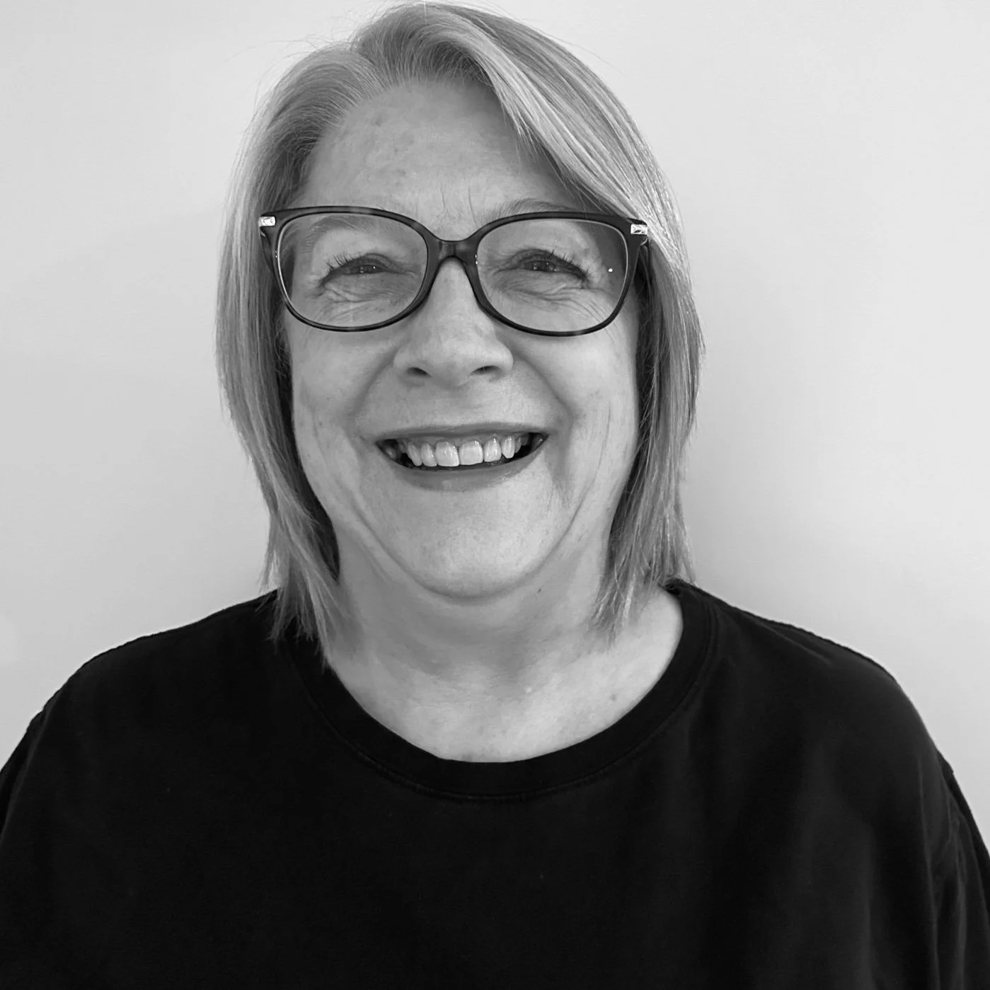 Smiling woman with glasses and short hairstyle in black and white portrait.