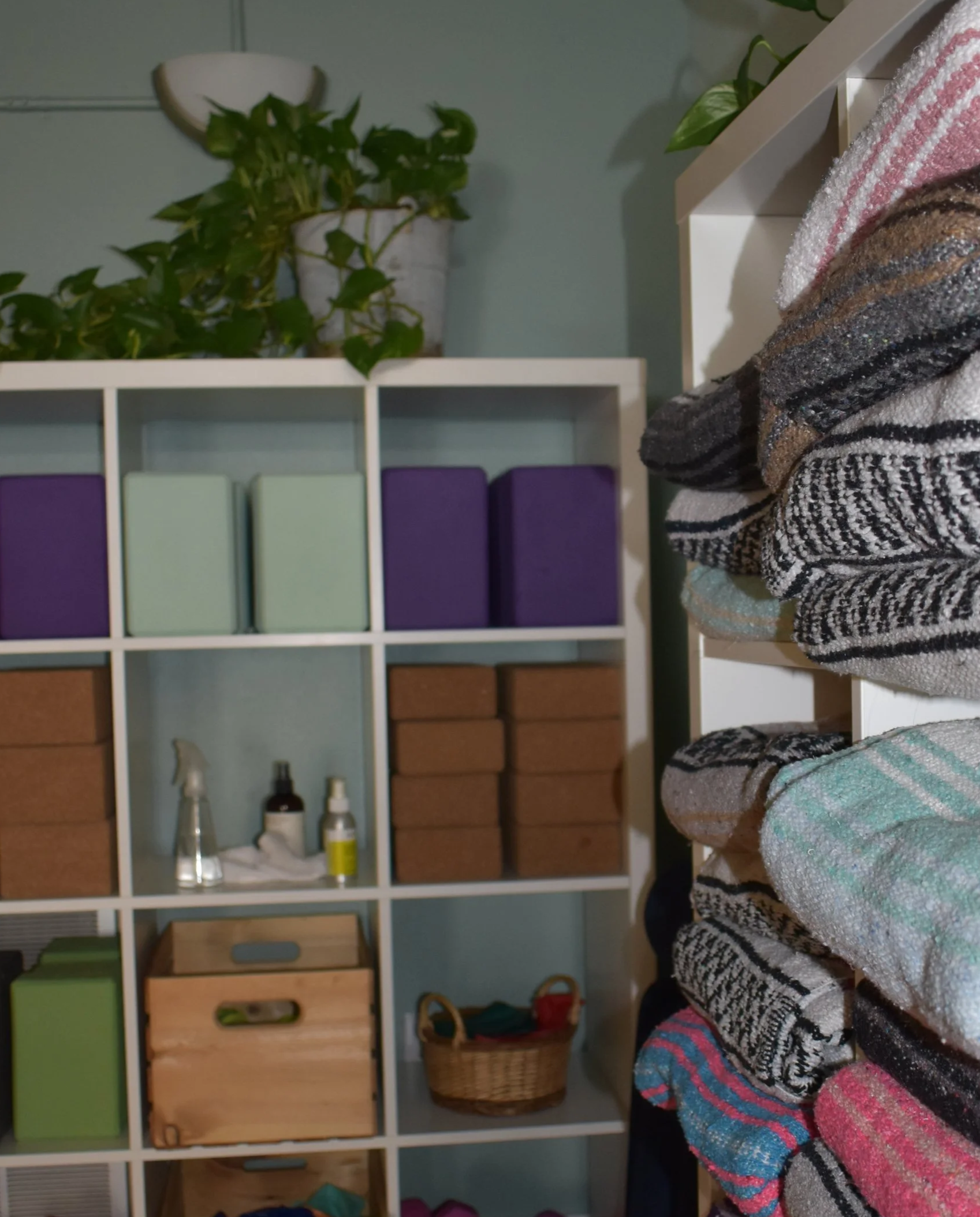 Part of a bookshelf with various storage boxes and baskets, visible bottles and tools, with a person wearing colorful striped clothing or a blanket in the foreground.