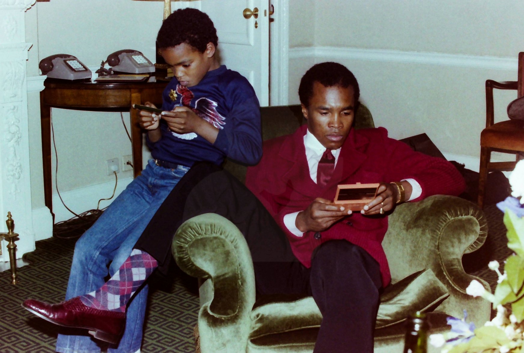 Ray Leonard Jr. and Sugar Ray Leonard playing hand held video games in their hotel room. London, England, 1982.