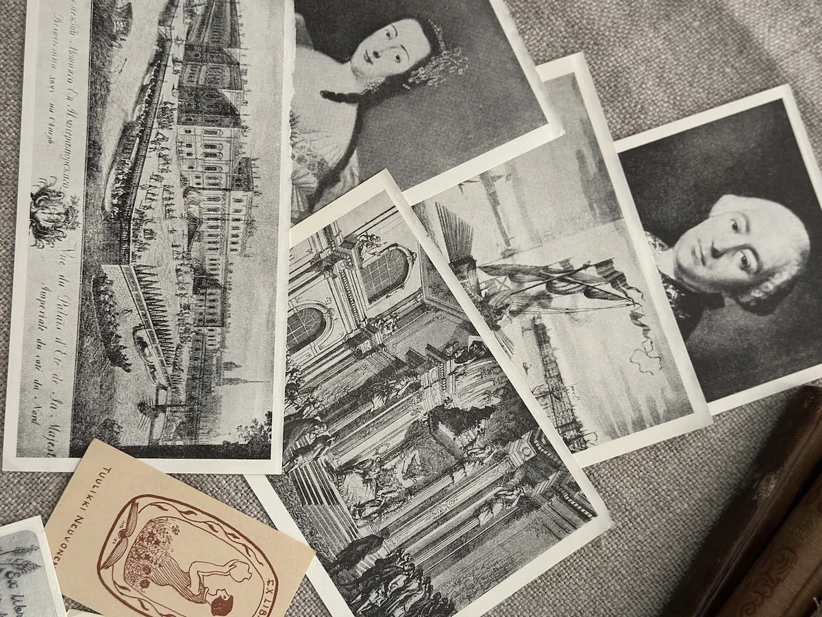 A collection of black and white vintage photographs and postcards spread out on a surface, including portraits of two women, a cityscape, and architectural details.