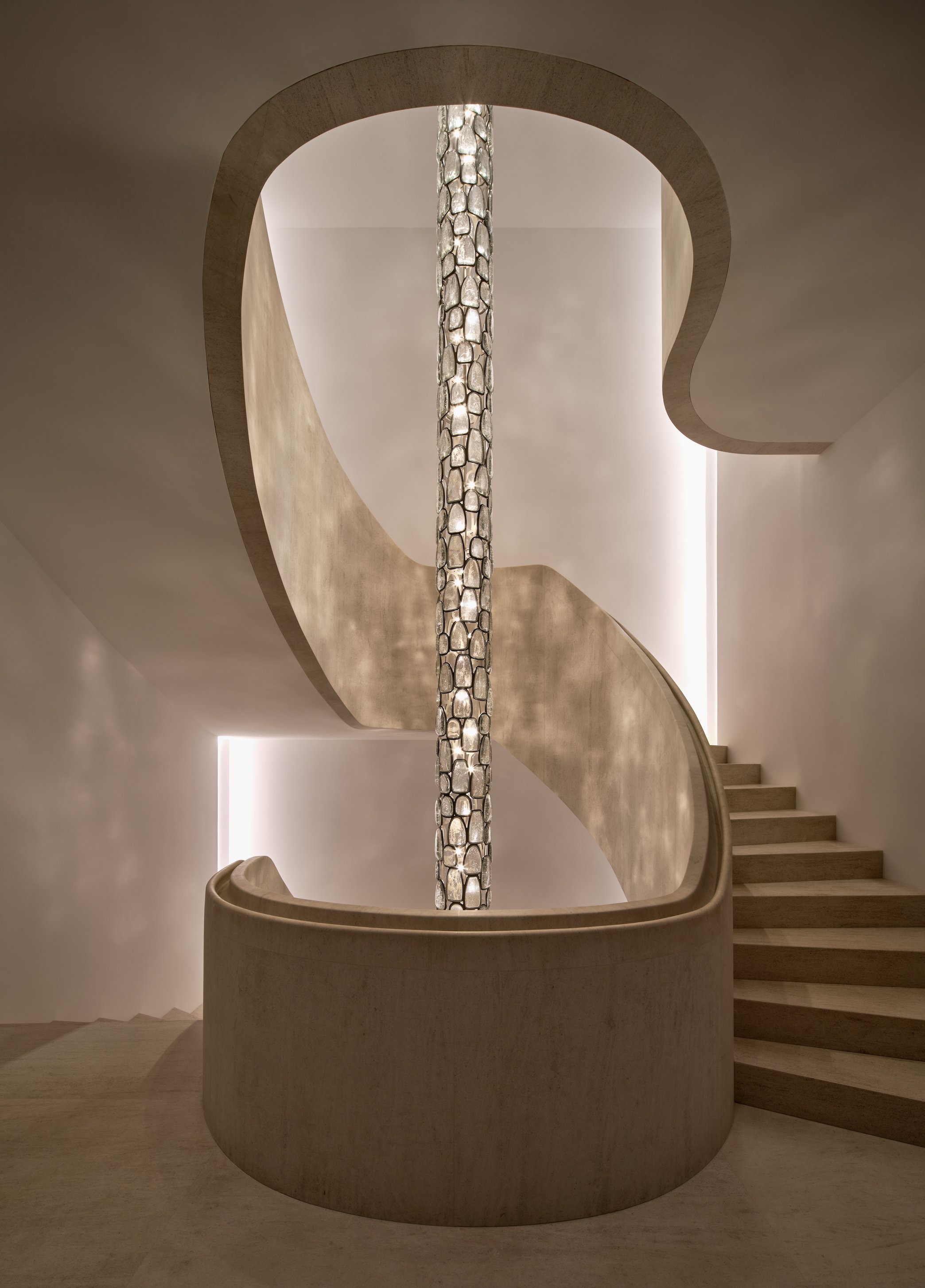 A modern, spiral staircase with a smooth wooden handrail and steps, viewed from below, featuring a central decorative column with enclosure stones.