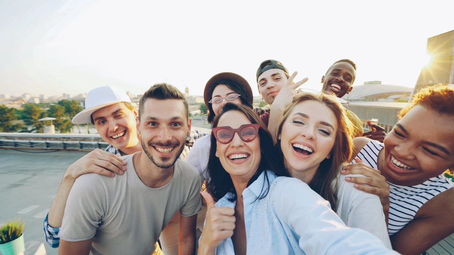 A group of smiling young adults taking a selfie together outdoors