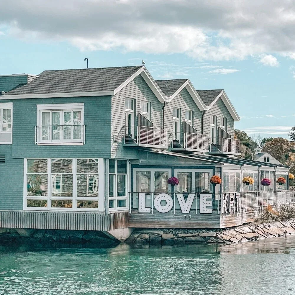 A gray-shingled waterfront building with a lit LOVE KPT sign on the harbor in Kennebunkport, Maine