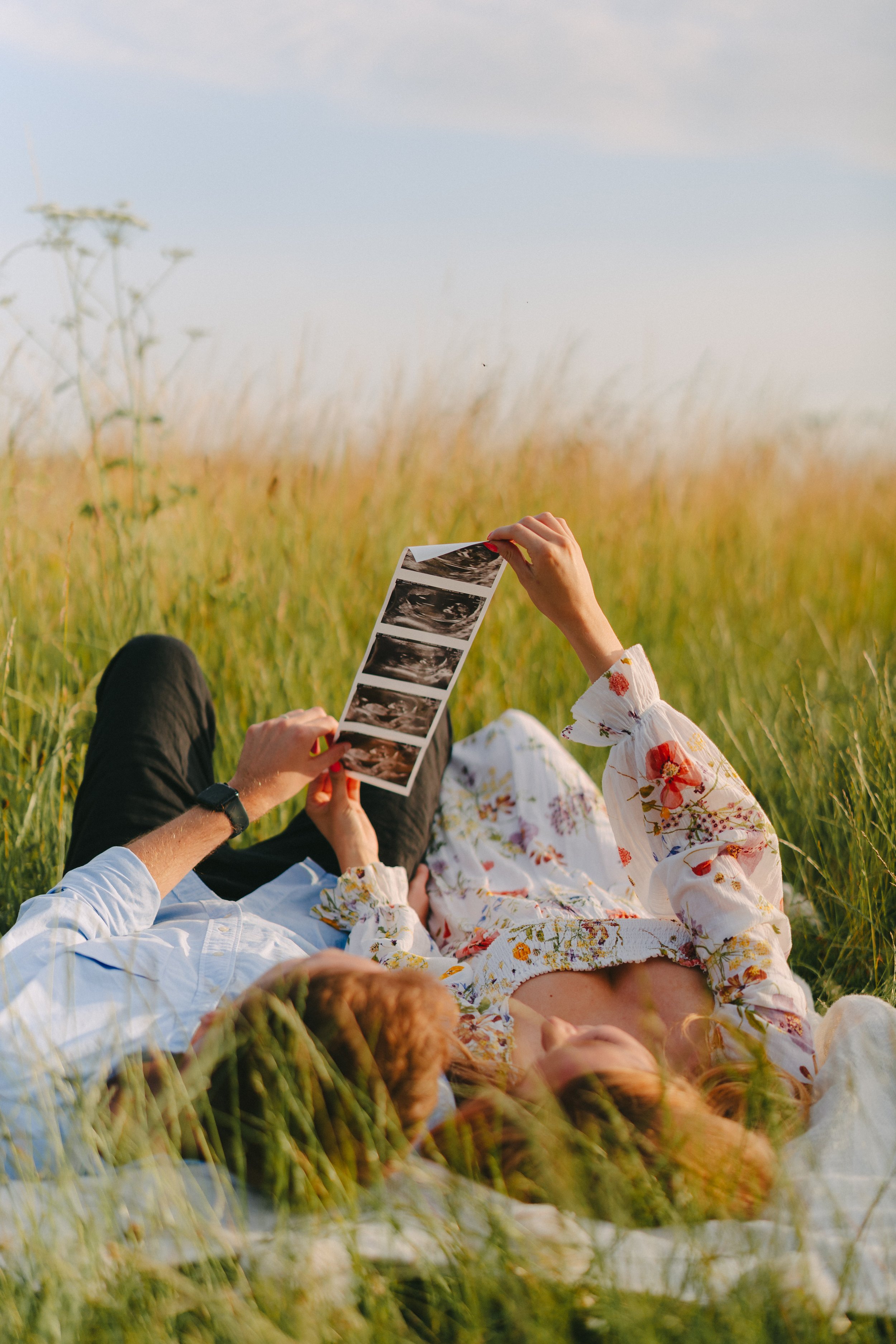 People sitting in a grassy field, holding and looking at ultrasound images.