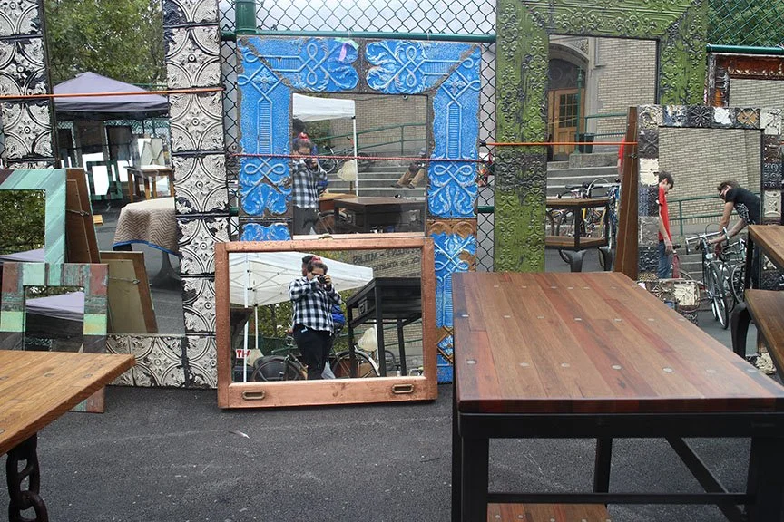 Display of various decorative mirrors and wooden tables outdoors at a market or shop.
