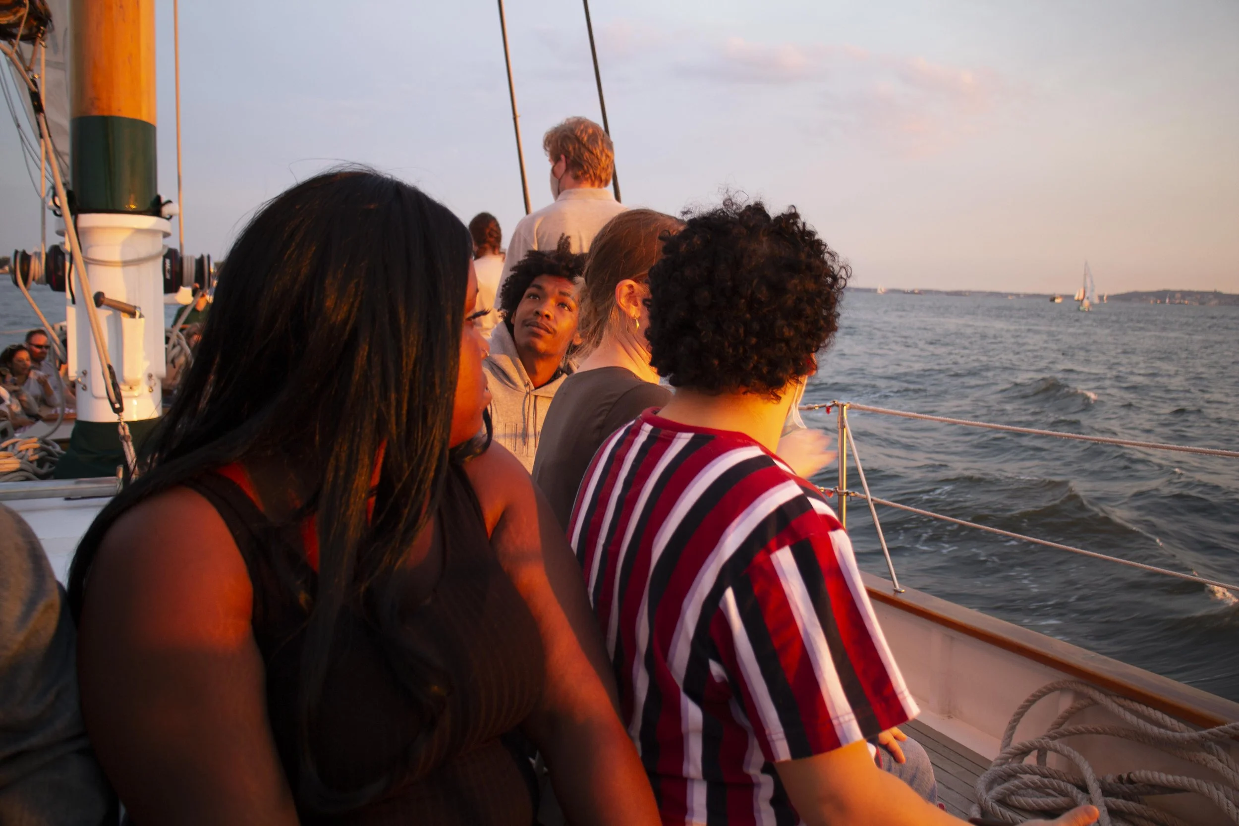 Group of people on a sailboat during sunset looking out at the water with sailboats in the distance.