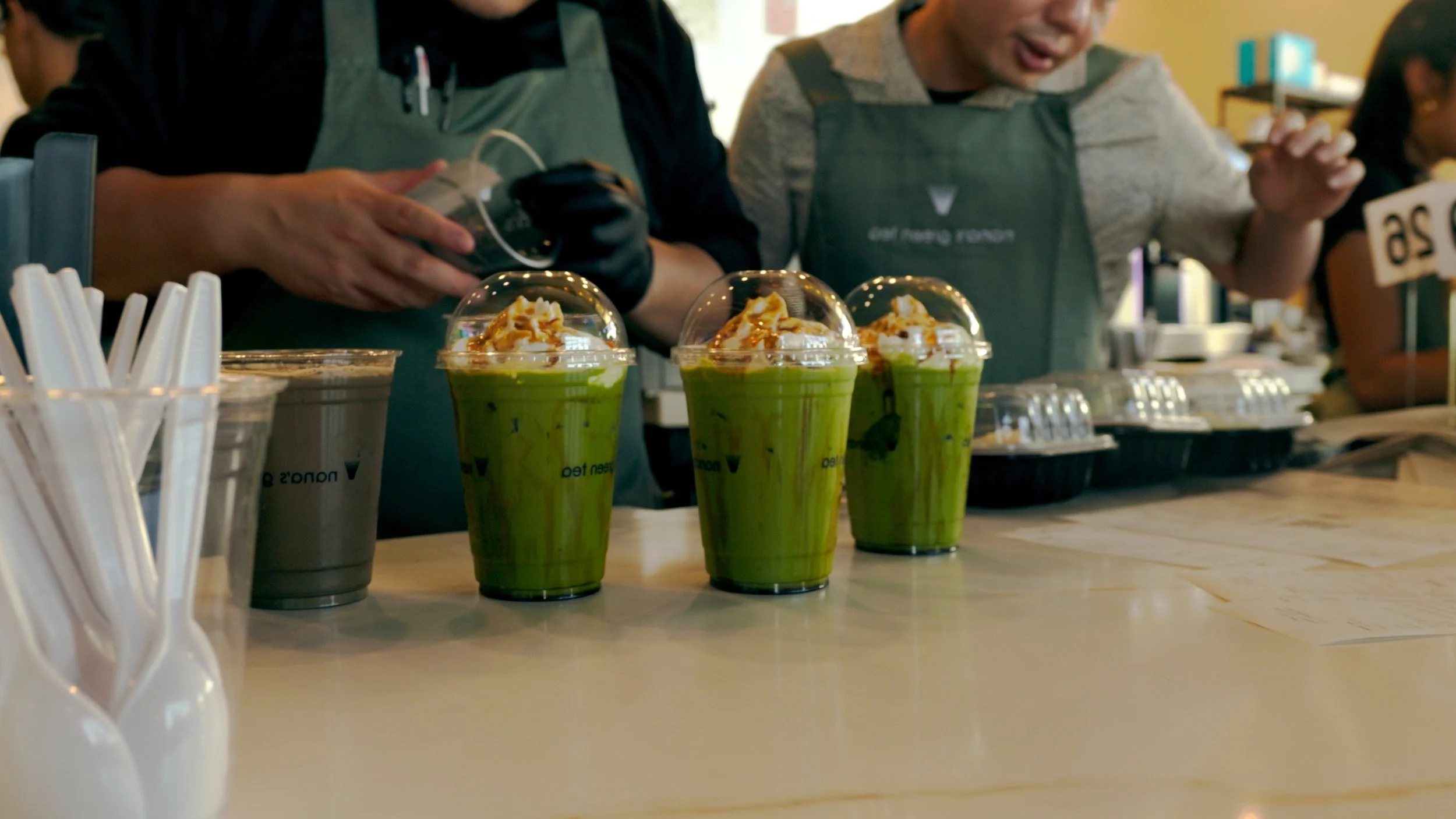 Three green matcha drinks with whipped cream and caramel drizzle on top, on a counter at a coffee shop.