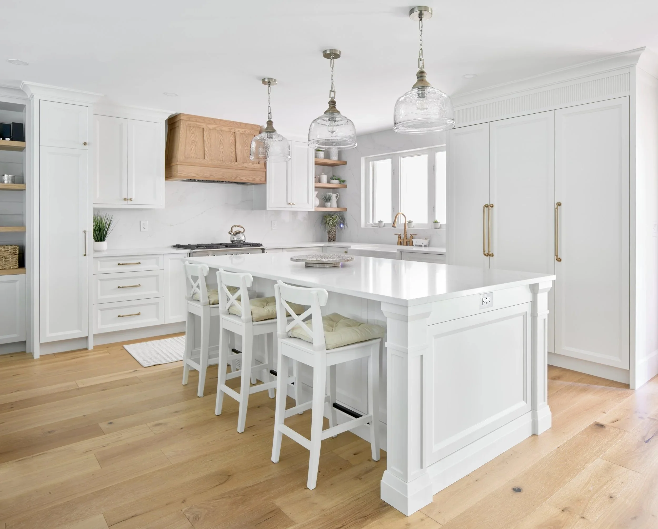 Modern white kitchen with wood accents, pendant lights, and a breakfast bar with white chairs