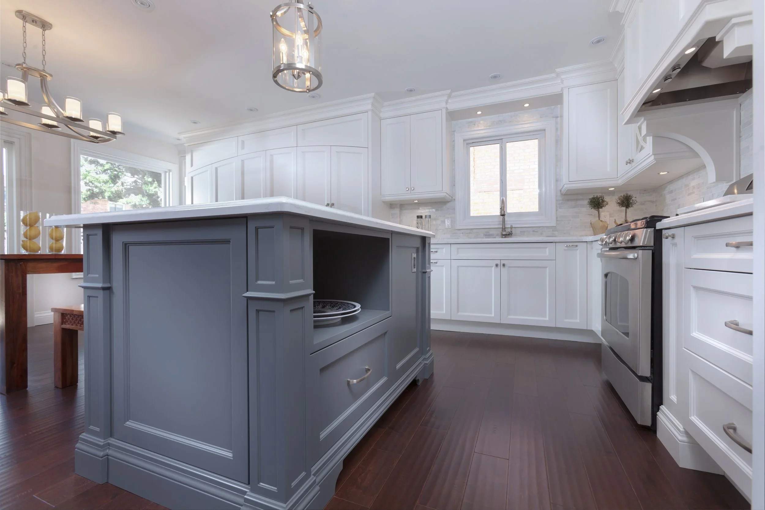 Modern kitchen with white cabinets, a blue kitchen island, large windows, and stainless steel appliances.