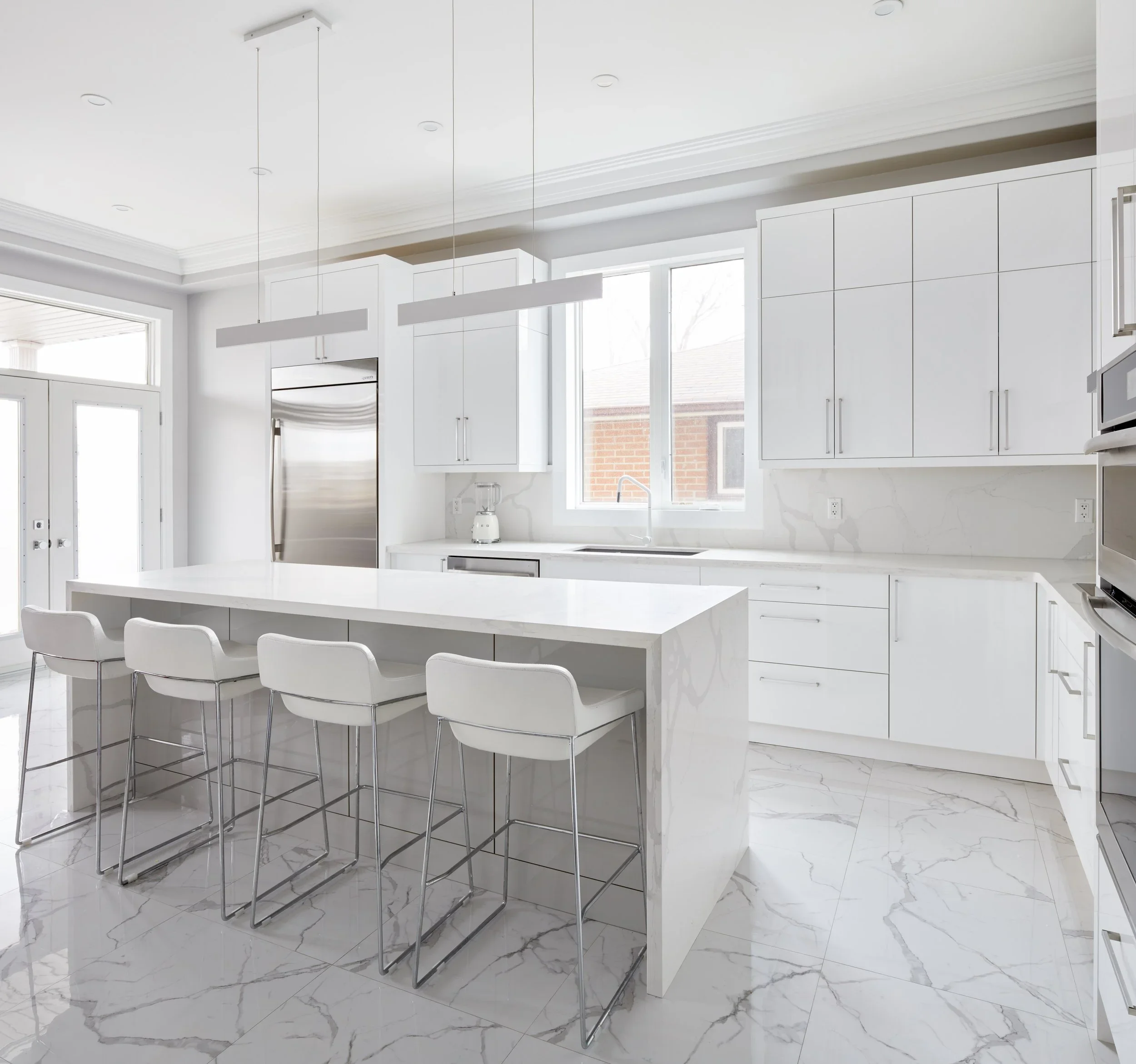 Modern white kitchen with marble floor, white cabinets, an island, and a hanging light fixture.