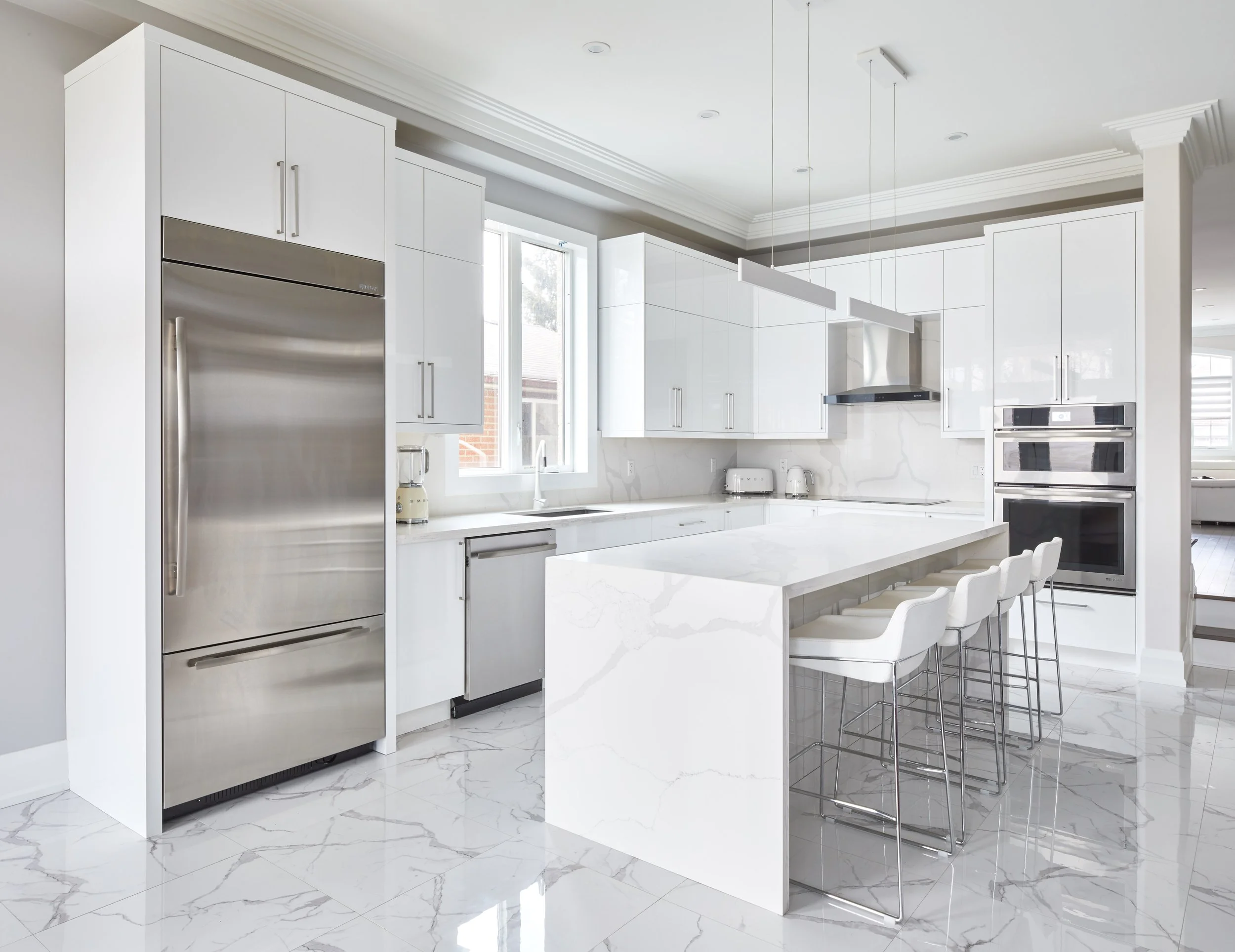 Modern white kitchen with marble flooring, stainless steel appliances, and a large island with bar stools.