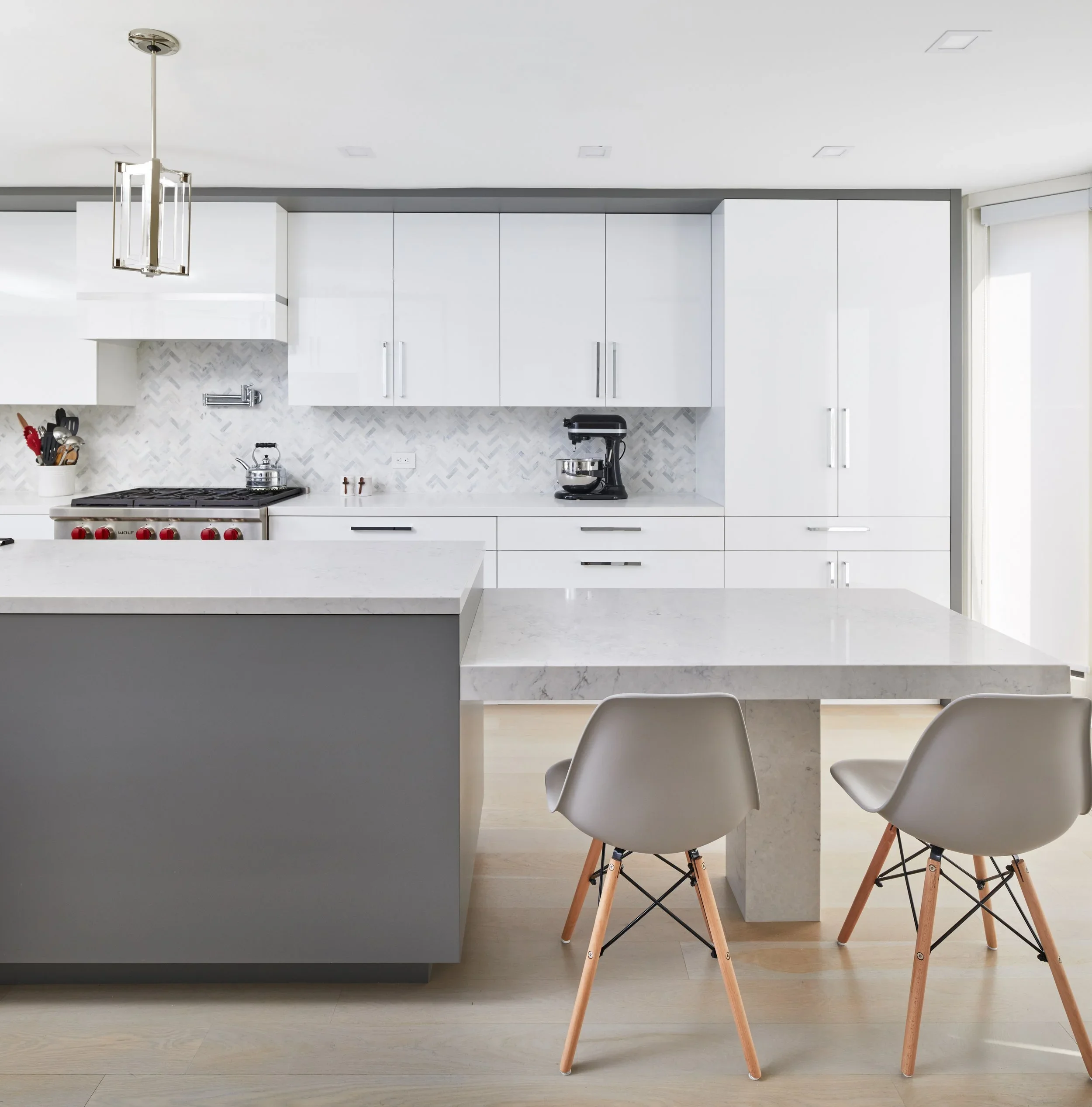 Modern kitchen with white cabinets, marble backsplash, black faucet, and a gray island with barstools.
