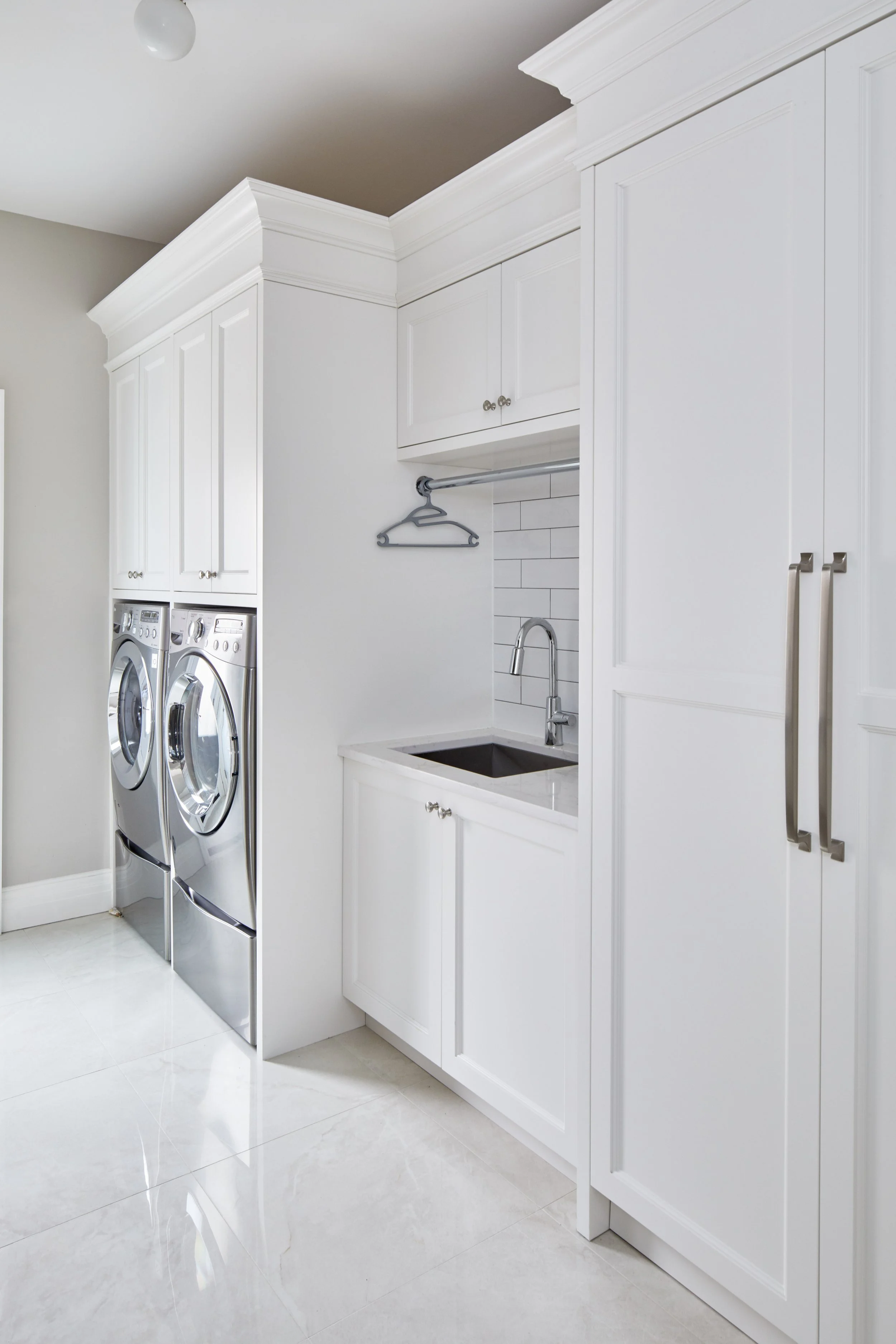 A modern laundry room with white cabinetry, a small sink, a chrome faucet, and a washing machine and dryer.